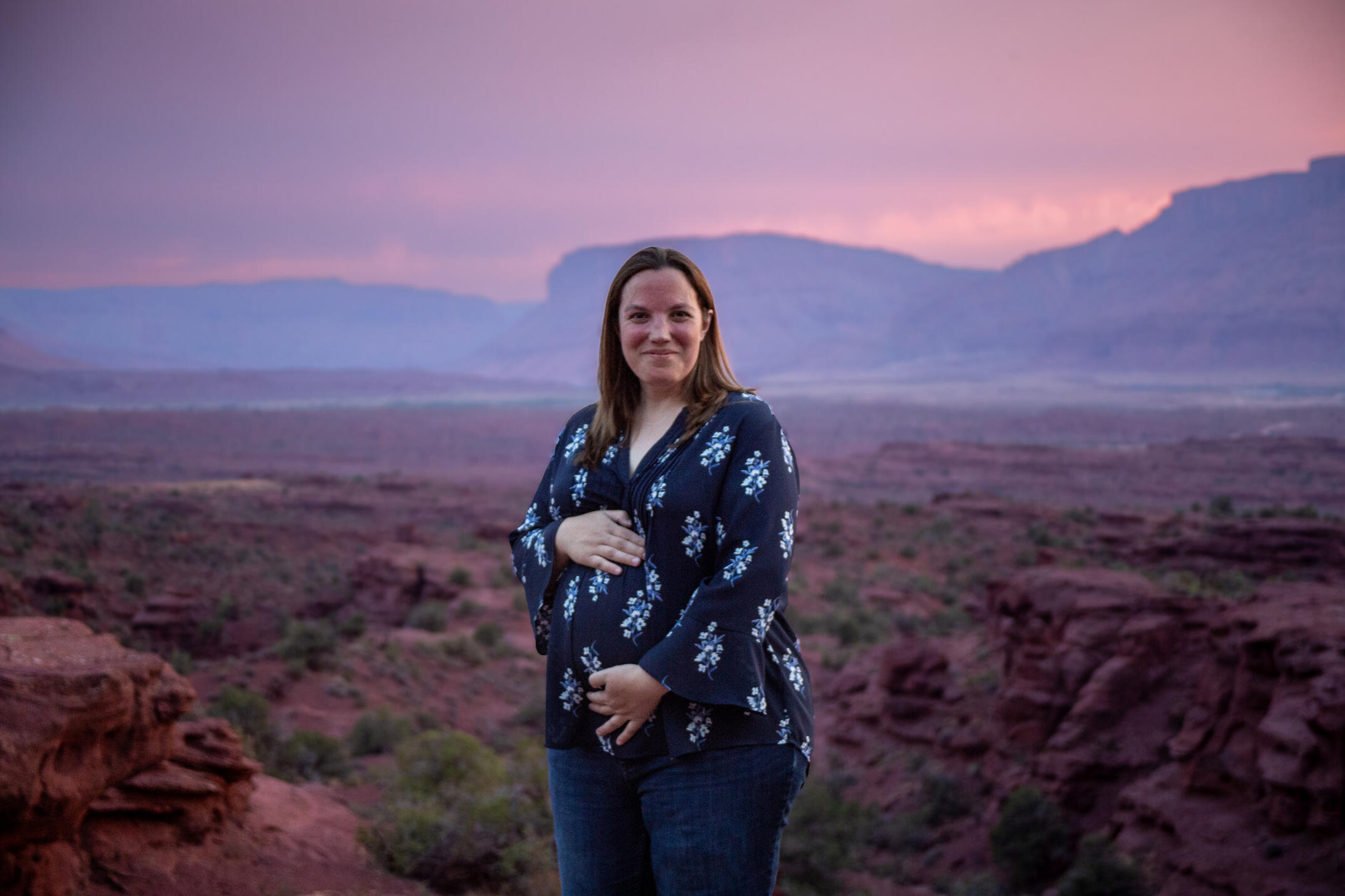 pregnant mom hold her belly with red rock background and beautiful purple sunset in background family photos baby announcement maternity